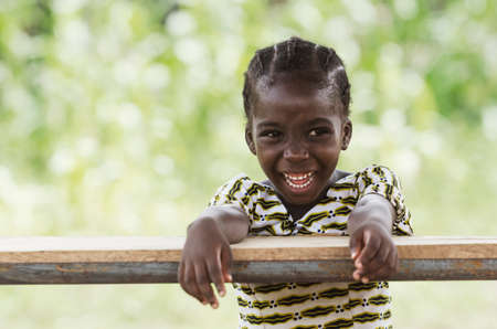Little african girl sitting at wooden table and smiling at camera with blurred backgroundの写真素材