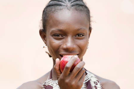 Happy young african girl eating apple and looking at camera