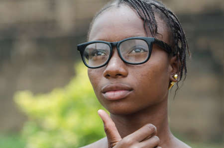Young african girl in eyeglasses thinking outdoors with blurred backgroundの写真素材