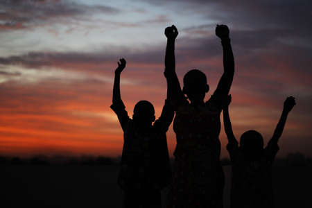 Three African Siblings Raising Their Hands Against A Colorful Evening Skyの写真素材