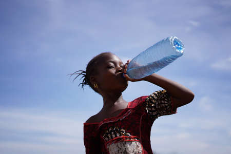 African Girl Drinking From a Water Bottle Under An Intensely Blue Skyの写真素材