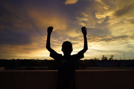Handsome African Boy Waves in front of Evening Sunの写真素材