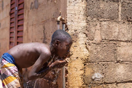 African child Washes His Body under Tap Water on a Sunny Hot Day