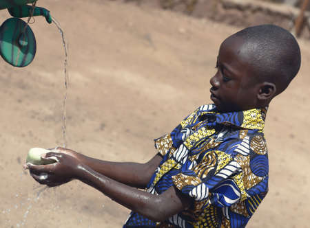 Outdoor Portrait of African Black Boy Washing Hands Outdoors to Fight Coronavirus Virus or Bacteriaの写真素材