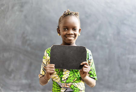 Cute African Black Girl Child in a School Uniform Holding Blackboard Sign with Copy Space as an Education School Symbolの写真素材