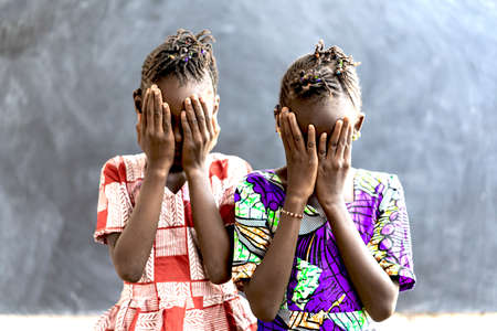 Beautiful African Children Girls Covering Faces in Sadness and Despairの写真素材