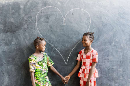 Two Cute African Girls Women Standing Together with Heart Love Symbol in Blackboard Backgroundの写真素材