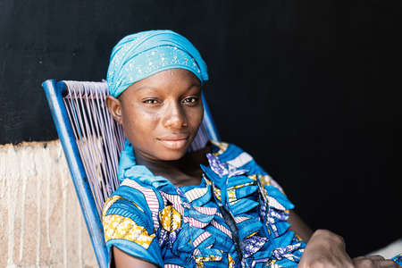Portrait of Adolescent Young College Girl Sitting in Chair with Blue Typical African Wax Dressの写真素材