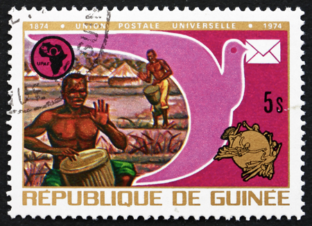 GUINEA - CIRCA 1974: a stamp printed in the Guinea shows Drummers, Pigeon, UPAF and UPU Emblems, Centenary of Universal Postal Union, circa 1974のeditorial素材