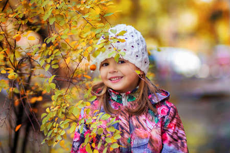 The girl in a jacket and in a cap costs near an autumn yellow bushの写真素材