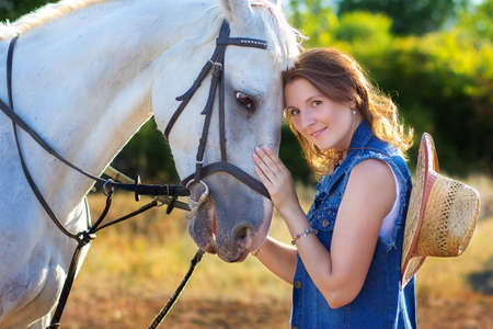 The girl's portrait with the hat embracing a white horseの写真素材