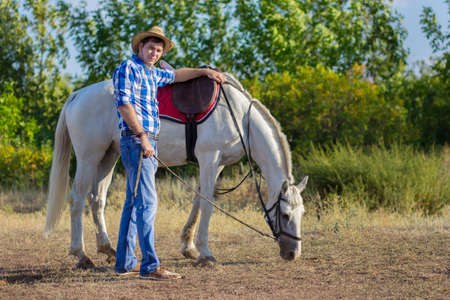 The man in a shirt and a hat walks with a horseの写真素材