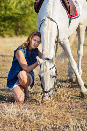 The girl sits near a white horse and embraces herの写真素材