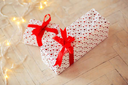 Two boxes in a gift box lie on a floor, tied up by a red tape, a garlandの写真素材