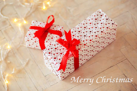Two boxes in a gift box lie on a floor, tied up by a red tape,. Inscription of the Merry Christmasの写真素材