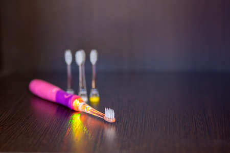 A battery-powered, pink-colored, electric pink toothbrush with three interchangeable nozzles lies on a shelf.の写真素材