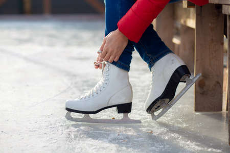A girl is tying shoelaces on figured white skates on an ice rinkの写真素材