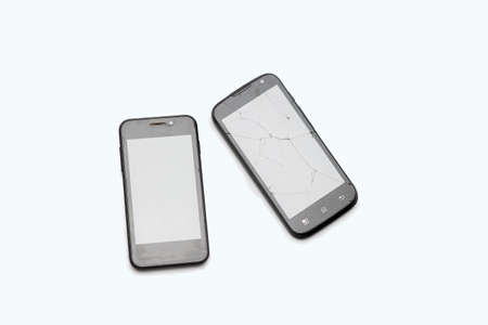 Two black phones lie on a white background. The broken smartphone. Cracks on the screenの写真素材