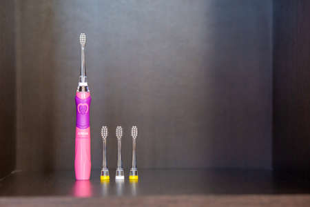 Children's electric pink toothbrush with backlight with three interchangeable nozzles stands on a dark shelfの写真素材