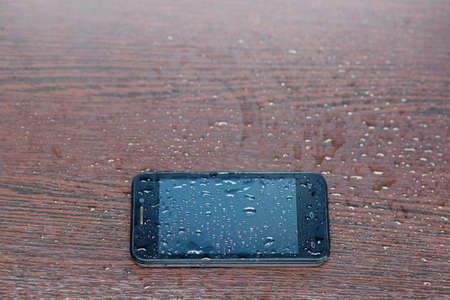 Black phone the smartphone lies on a wooden background, splashed by water drops.の写真素材