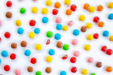 Scattered multi-colored small round candies. Pattern of chocolate dragees in multi-colored glaze on a white backgroundの写真素材