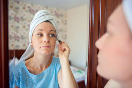 A girl with a towel on her head paints her eyelashes with mascara.の写真素材