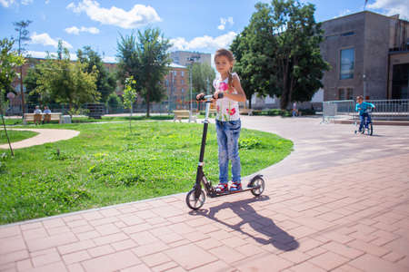 A child in torn jeans rides a scooter in a summer park. Modern childhoodの写真素材