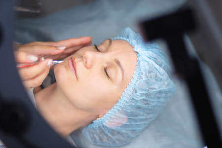 Preparation for permanent lip makeup. Drawing the contour of the lips for tattooing. Woman makes a tattoo on her faceの写真素材