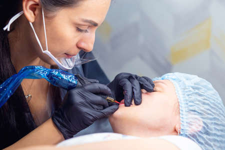 A woman makes permanent lip makeup to another woman in a beauty salon cabinet. Face tattoo. Modern trends in cosmetologyの写真素材