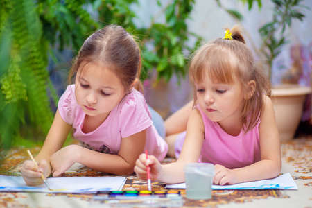 Two girls paint with paints lying on the floor at home or in kindergarten. Children's creativityの写真素材
