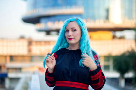 A woman with blue hair in a black dress walks through the city.の写真素材