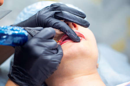 The process of applying permanent makeup on the lips with a tattoo machine close-up. Permanent...