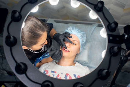 A woman makes permanent lip makeup to another woman in a beauty salon cabinet.の写真素材