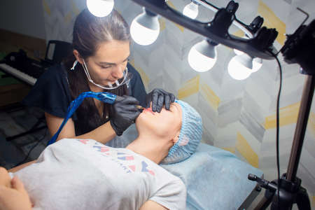 A woman makes permanent lip makeup to another woman in a beauty salon cabinet.の写真素材