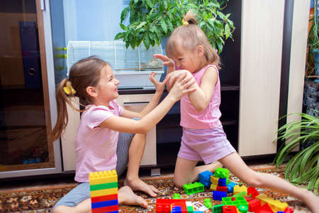 Two girls sisters play at home in a colored plastic construction set, argue about something and fightの写真素材