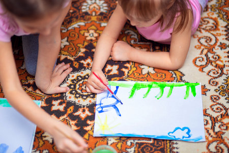 Children at home paint with watercolors lying on the floorの写真素材