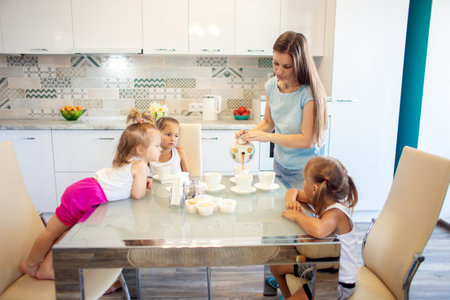 A mother of many children in the kitchen pours tea for her children from a teapotの写真素材