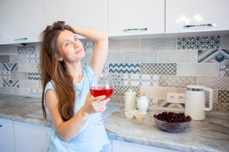 Young woman at home in the kitchen alone drinking wine and smiling happilyの写真素材