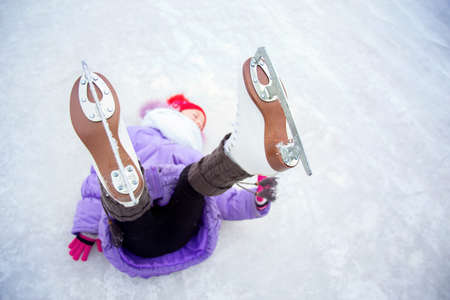 A girl, shod in figure skates, lies on the ice with her legs raised, focus on skates. Winter funの写真素材