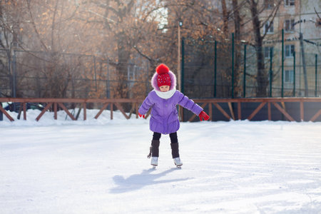 A girl skates on an ice rink in winter. Skating rink in the courtyard in the city. Child learns to...
