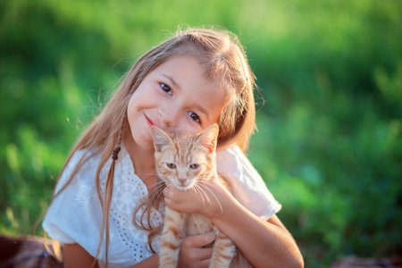 The girl plays with a ginger kitten on the street. Country girl playing with a cat. Child resting on the farmの写真素材