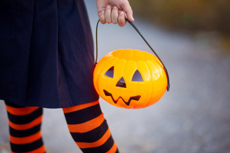 A girl in striped gaiters holds a candy bowl in the form of a pumpkin for Halloween. Carnival outfit for Halloween. Trick or treat. close-up pumpkinの写真素材