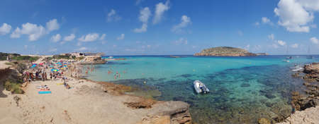 San Antonio, Ibiza - 07/14/2018: Panoramic view of Cala Comte beach in Spain during summer with a crispy clear turquoise sea water and people laying down on the sand beachの写真素材