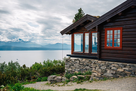 Scenic Mountain Cabin Overlooking Serene Lake and Majestic Snow-Capped Peaks Amidst Lush Greenery...