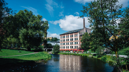 Charming Historical Industrial Building by a Tranquil Riverside Park Under a Clear Blue Sky