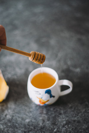 Refreshing Honey Drizzle Into Cartoon Character Mug Filled With Warm Tea on Dark Granite Surface