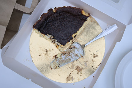 Half Eaten Burnt Cheesecake in Box with Knife on Golden Tray White Background
