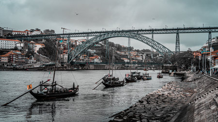 Serene Riverfront Scene with Historic Boats and Iconic Arched Bridge in Picturesque European...
