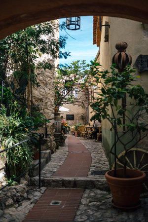 Charming European Alleyway Lined with Lush Greenery Leading to a Cozy Outdoor CafÃ© Under a Clear...