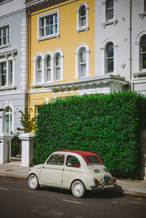 Vintage Car Parked on a Charming Street with Classic Architecture and Vibrant Hedges on a Sunny Day